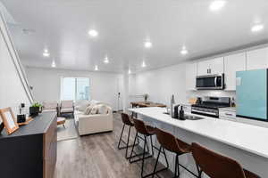 Kitchen featuring appliances with stainless steel finishes, a breakfast bar, sink, white cabinets, and light hardwood / wood-style floors