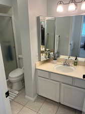 Bathroom featuring an enclosed shower, vanity, tile patterned floors, and toilet