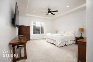 Bedroom featuring ceiling fan, light colored carpet, and a tray ceiling