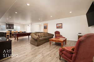 Living room featuring pool table, a textured ceiling, and light wood-type flooring