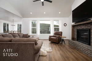 Living room featuring lofted ceiling, hardwood / wood-style floors, ceiling fan with notable chandelier, and a fireplace