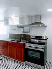 Kitchen featuring stainless steel range with electric cooktop, sink, wall chimney exhaust hood, and backsplash