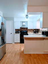 Kitchen with appliances with stainless steel finishes, sink, light hardwood / wood-style floors, wall chimney exhaust hood, and white cabinets