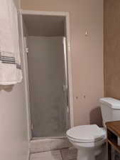 Bathroom featuring toilet, a shower with shower door, and tile patterned flooring