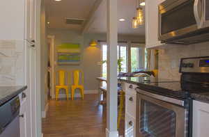 Kitchen with stainless steel appliances, white cabinetry, pendant lighting, and dark stone counters