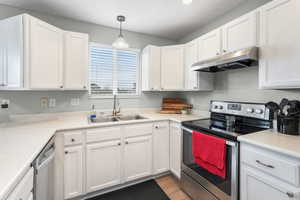 Kitchen featuring hanging light fixtures, appliances with stainless steel finishes, sink, and white cabinets, LVP