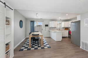 Kitchen featuring white cabinetry, a center island, hanging light fixtures, appliances with stainless steel finishes and Luxury Vinyl Planking