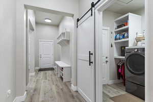 Laundry room with a barn door, washer / dryer, and light hardwood / wood-style flooring