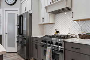 Kitchen featuring premium range hood, white cabinetry, high end appliances, light hardwood / wood-style floors, and decorative backsplash