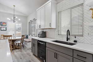 Kitchen featuring decorative light fixtures, dishwasher, sink, white cabinets, and light stone countertops