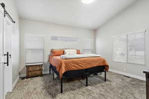 Carpeted bedroom featuring a barn door and lofted ceiling