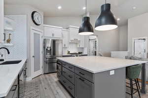 Kitchen featuring sink, appliances with stainless steel finishes, white cabinetry, hanging light fixtures, and light stone counters