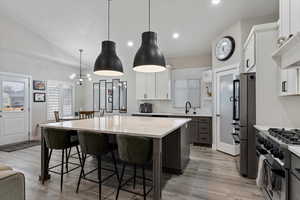 Kitchen featuring sink, stainless steel appliances, white cabinets, a kitchen island, and decorative light fixtures