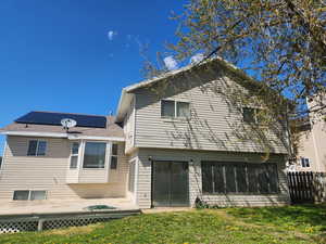 Rear view of property featuring a wooden deck, a yard, roof mounted solar panels, and fence