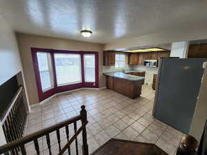 Kitchen featuring appliances with stainless steel finishes, sink, light tile patterned floors, a textured ceiling, and kitchen peninsula