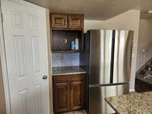 Kitchen featuring light stone countertops, open shelves, tasteful backsplash, a textured ceiling, and freestanding refrigerator
