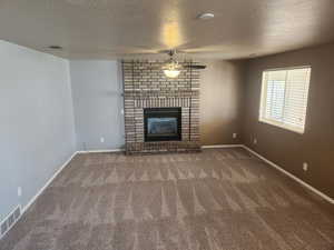 Unfurnished living room with a textured ceiling, carpet floors, visible vents, and a ceiling fan