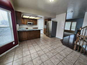 Kitchen with light tile patterned flooring, a healthy amount of sunlight, appliances with stainless steel finishes, and kitchen peninsula