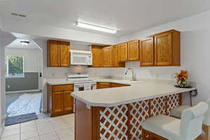 Kitchen featuring sink, white appliances, kitchen peninsula, and a kitchen bar