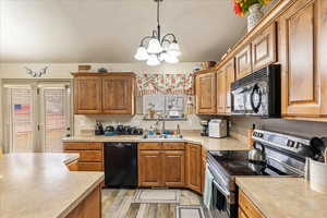 Kitchen featuring decorative light fixtures, sink, a chandelier, black appliances, and light wood-type flooring