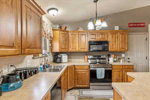 Kitchen featuring sink, decorative light fixtures, vaulted ceiling, a notable chandelier, and black appliances