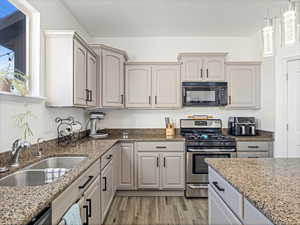 Kitchen featuring a wealth of natural light, sink, gas range, light stone countertops, and light wood-type flooring