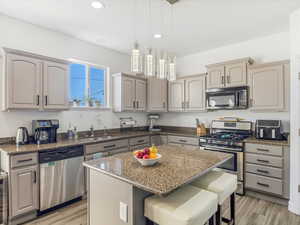 Kitchen featuring hanging light fixtures, light wood-type flooring, dark stone countertops, a kitchen island, and stainless steel appliances