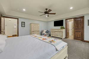 Carpeted bedroom featuring a tray ceiling and ceiling fan