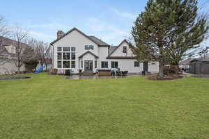 Back of house featuring a patio area, a hot tub, a playground, and a lawn