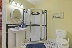 Bathroom with an enclosed shower, sink, tile walls, and toilet