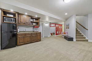 Kitchen featuring black refrigerator, sink, light stone counters, and light carpet