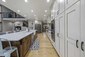 Kitchen featuring white cabinetry, light hardwood / wood-style flooring, a large island with sink, appliances with stainless steel finishes, and a kitchen breakfast bar