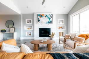 Living room featuring lofted ceiling, hardwood / wood-style flooring, a large fireplace, and ceiling fan