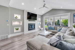 Living room with ceiling fan, lofted ceiling, a large fireplace, and light hardwood / wood-style floors