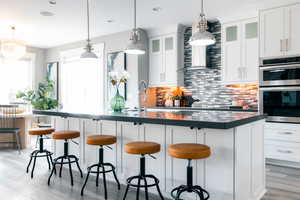 Kitchen with backsplash, stainless steel double oven, a center island with sink, and white cabinets