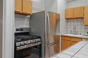 Kitchen with gas range, tile counters, sink, and backsplash