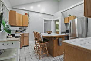 Kitchen featuring tile countertops, decorative backsplash, a center island, light tile patterned floors, and stainless steel appliances