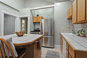 Kitchen featuring sink, decorative backsplash, tile counters, light tile patterned floors, and stainless steel appliances