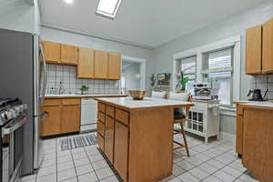 Kitchen featuring light tile patterned flooring, dishwasher, sink, a kitchen bar, and stainless steel gas range