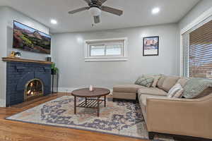 Living room with hardwood / wood-style flooring, a brick fireplace, and ceiling fan