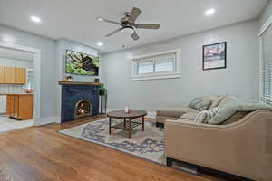 Living room with a fireplace, light hardwood / wood-style flooring, and ceiling fan