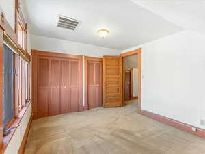 Unfurnished bedroom with vaulted ceiling, light colored carpet, and multiple closets