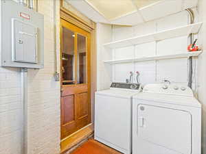 Laundry room with brick wall, washer and dryer, and electric panel