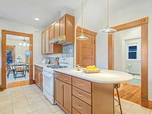 Kitchen featuring light tile patterned flooring, decorative light fixtures, white range with gas cooktop, a kitchen breakfast bar, and kitchen peninsula