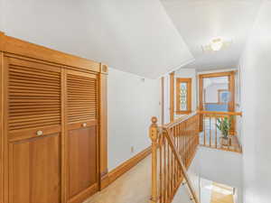 Hall featuring vaulted ceiling and light carpet