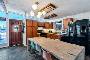 Kitchen with a textured ceiling, sink, hanging light fixtures, and black appliances