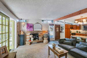 Living room featuring a stone fireplace, sink, a textured ceiling, and beam ceiling