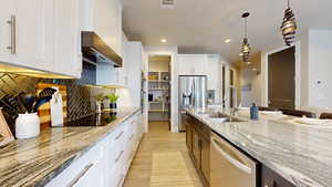 Kitchen with sink, light stone counters, decorative light fixtures, stainless steel appliances, and white cabinets