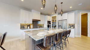 Kitchen with appliances with stainless steel finishes, an island with sink, white cabinets, hanging light fixtures, and light stone countertops