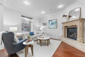 Living room with a high end fireplace, wood flooring, and ornamental molding